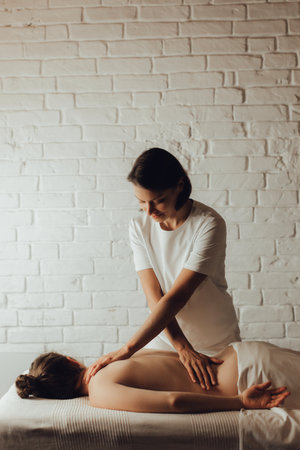 Hands of female chiropractor massaging back of young woman lying on massage table on white background. Visceral massage. Concept of physical therapy treatment, neck pressure point.の写真素材