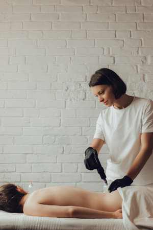 Hands of female chiropractor massaging back of young woman lying on massage table. Masseuse applying...