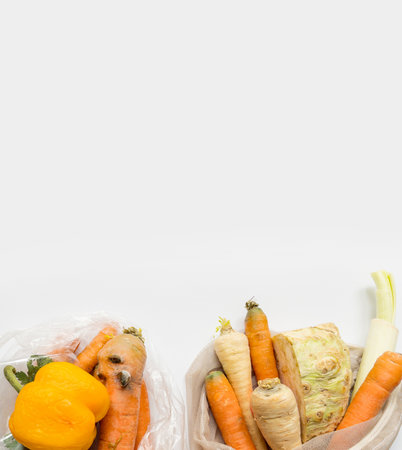Vegetables from local market in reusable shopping bag and rotten spoiled vegetables in plastic shopping bag over light background. Top view. Organic food. Plastic Pollution, Ethical Consumerism.の写真素材