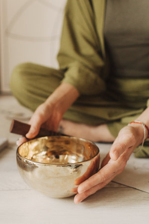 Close up photo of woman hands holding playing on Tibetan singing bowl while sitting on yoga mat. Vintage tonned. Soft focus, blurred and noise effect.の写真素材