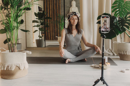 Live streaming on a smartphone - online yoga lesson. Beautiful woman training at home and watching online lessons in the digital tablet. Vintage tonned. Soft focus blurred and noise effect.の写真素材