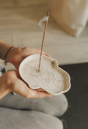 A young woman lighting incense sticks an home before yoga. Buddhist healing practices. Clearing the space of negative energy. Aromatherapy. Selective focus.の写真素材