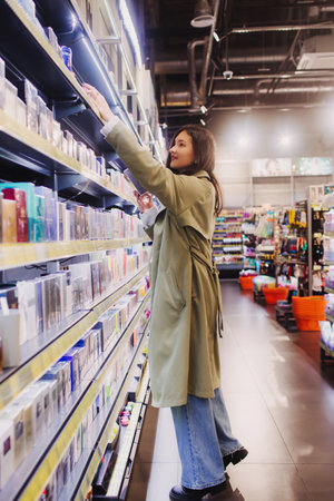 Young girl shopping in retail store. Beautiful teenage testing and buying cosmetics in a beauty store. Side view. Personal care and modern cosmetology. Beauty and fashion. Retail and consumerism.の写真素材