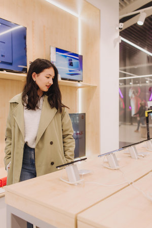 Korean teenage girl choosing phone at technology store. Female customer viewing smart phones in...