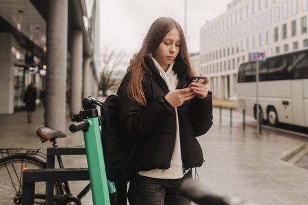School age girl renting an electric scooter or bicycle using smartphone, making contactless payment...