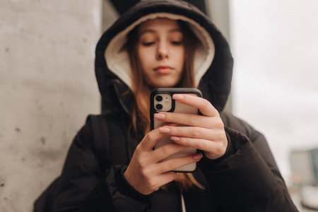 Half length portrait of girl in casual wear holding smartphone for blogging in the city in the...