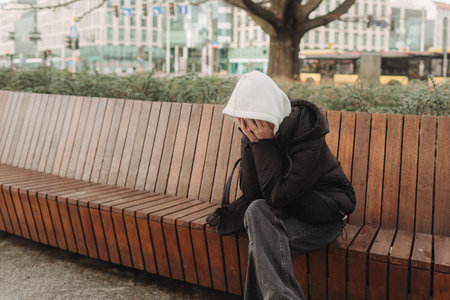 Upset and depressed girl holding smartphone and holding head. University sad student suffering from depression at high school. Lonely bullied teen.の写真素材
