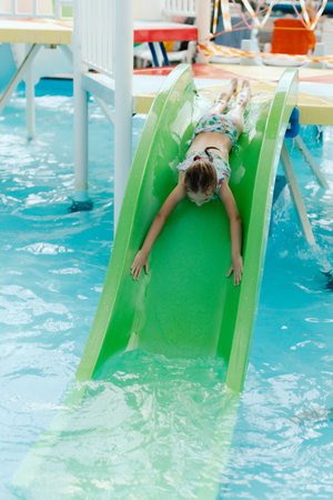 Little girl slides down a slide into a pool at a aquapark. Happy child having fun in water, beach...