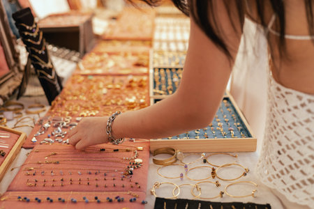 Female shopper picks out a handcrafted jewelry from a collection on a market stall. Small business...