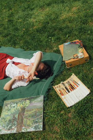 Female artis paints a picture in the park. Mindfulness, art therapy, creativity concept. Process of plein air painting in nature. A series of photos showing the step-by-step creation of a painting.の写真素材