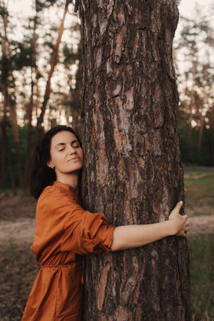 Happy adult lady hug tree trunk in outdoor leisure park activity. Concept of environment and ambient nature care. People love planet earth and stop deforestation lifestyleの写真素材