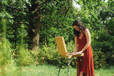 Female artis paints a picture in the park. Mindfulness, art therapy, creativity concept. Process of plein air painting in nature. A series of photos showing the step-by-step creation of a painting.の写真素材