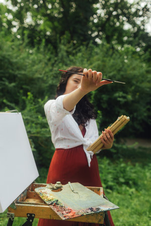 Female artis paints a picture in the park. Mindfulness, art therapy, creativity concept. Process of plein air painting in nature. A series of photos showing the step-by-step creation of a painting.の写真素材