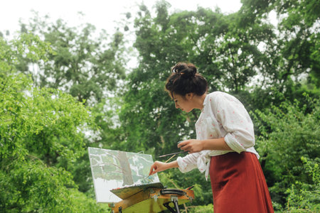 Female artis paints a picture in the park. Mindfulness, art therapy, creativity concept. Process of plein air painting in nature. A series of photos showing the step-by-step creation of a painting.の写真素材