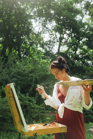 Female artis paints a picture in the park. Mindfulness, art therapy, creativity concept. Process of plein air painting in nature. A series of photos showing the step-by-step creation of a painting.の写真素材