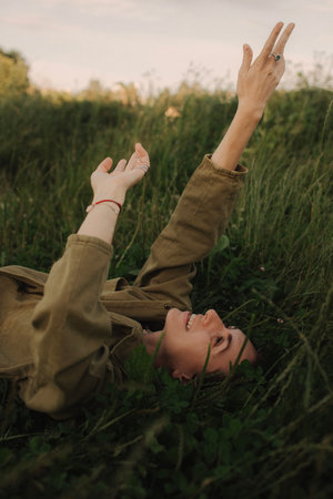 Beautiful cute woman no makeup in white shirt laying down on green grass with white flowers. Wild nature, mood vacation, relax. Top view of girl. Be free, love forest. Part of the series.の写真素材