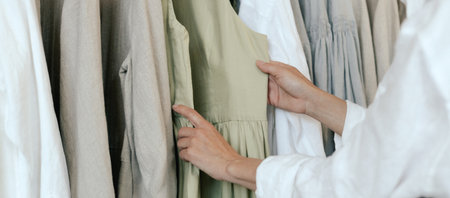 Close-up of female hands plucked hanger choosing clothes in clothing store. Middle aged woman runs across a rack of clothes in a shopping mall. Sale promotion and shopping concept. Part of the series.の写真素材