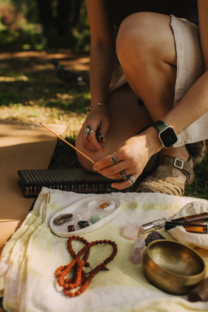 Close up of female hands lighting incense sticks in park before yoga. Buddhist healing practices....