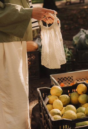 Close up lady's hands with a reusable shopping bag. Woman shopping at the local Farmers market. Beautiful woman buying vegetables. Close up. Part of the series.の写真素材