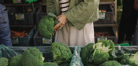 Close up of woman buying green broccoli on the local Farmers market. Mature Female Customer Shopping At Farmers Market Stall. Close up. Part of the series.の写真素材