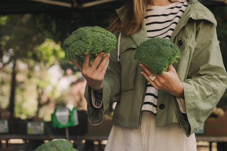 Close up of woman buying green broccoli on the local Farmers market. Mature Female Customer Shopping At Farmers Market Stall. Close up. Part of the series.の写真素材