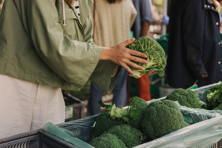 Close up of woman buying green broccoli on the local Farmers market. Mature Female Customer Shopping At Farmers Market Stall. Close up. Part of the series.の写真素材