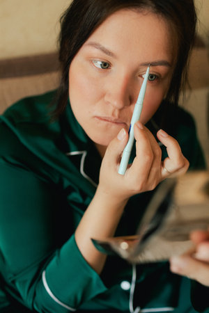Plus size woman applying makeup on face with brush while recording vlog on smartphone for social...
