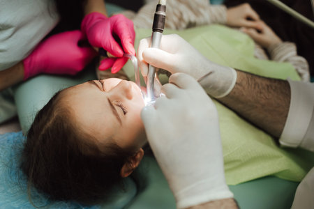 Cropped portrait of little girl with pigtails hair sitting in dental chair looking at camera. A doctor in gloves holds examination tools. Children's dentistry. Part of a series.の写真素材