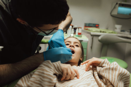 Cropped portrait of little girl with pigtails hair sitting in dental chair looking at camera. A doctor in gloves holds examination tools. Children's dentistry. Part of a series.の写真素材