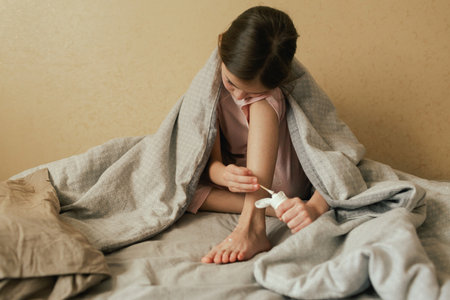 A sick child with skin rashes applies cream from itchy spots on her skin in bed. Allergic reaction, Drug allergy, Scarlet fever, Atopic dermatitis, Diaper rash, Urticaria, Scabies. Part of a series.の写真素材
