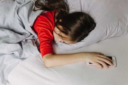 Pretty teenage girl lying under covers on bed. Getting up early in the morning, the overslept school. The alarm is waking herm up. Generation alpha and new day concept. Part of a seriesの写真素材