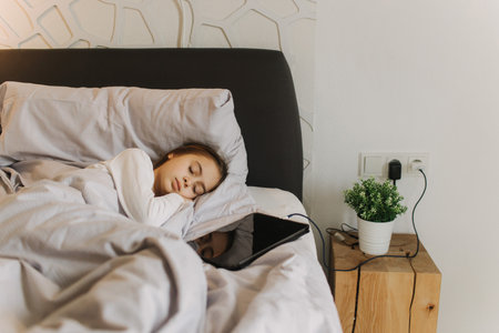Pretty teenage girl fell asleep with a tablet in her hands, secretly watching movie, playing online games, lying under covers on bed. Generation alpha concept. Part of a seriesの写真素材