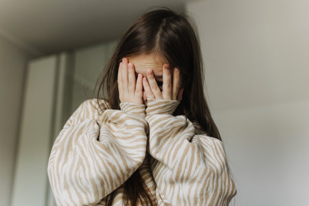 Photo of Expression of lonely female teenager at home. Pensive teen. A pretty teenage girl covers her face with her hands. Depression, teen depression, pain, suffering, mental health.の写真素材