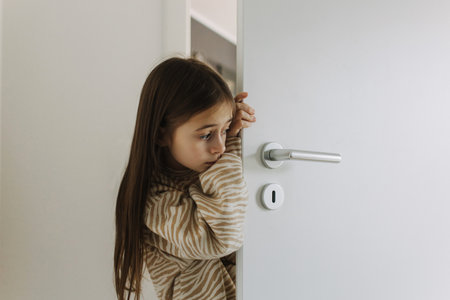 Photo of Expression of lonely female teenager at home. Pensive teen. A pretty teenage girl is hiding behind the door. Depression, teen depression, pain, suffering, mental health.の写真素材