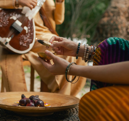 Indian musician in traditional clothes playing sitar festive season outdoor home. Woman in traditional saree hand lighting Diya lamp during Diwali festival. Happy greeting photo. Part of a series.の写真素材