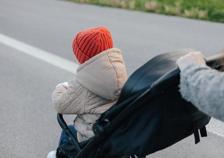 Close up of young mother in warm coat pushing baby stroller and slowly crossing street on crosswalk....