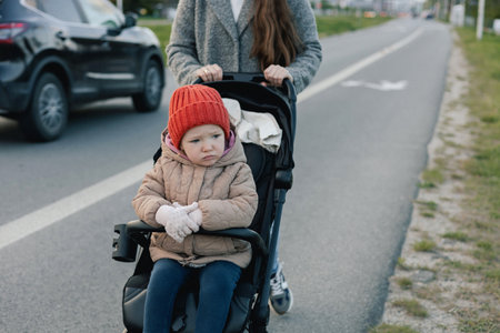 Close up of young mother in warm coat pushing baby stroller and slowly crossing street on crosswalk....