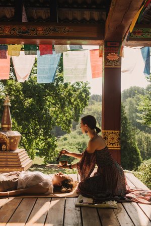 Close up of female mentor and student before Mindful meditation and yoga in the gazebo. Facilitating meditative experience. Part of the series. Tibetan singing bowl. Soft focus, blurred, noise effectの写真素材