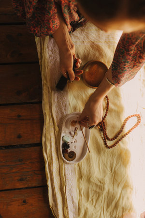 Hands arranging meditation items including prayer beads and bowls on a light fabric surface against...