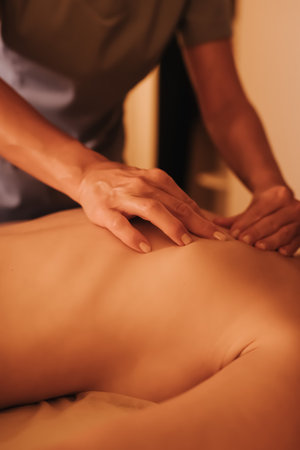 Hands of female chiropractor massaging shoulders of young woman lying on massage table. Concept of...