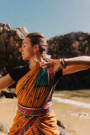 Indian woman in traditional saree clothes dances traditional dances on the nature with the ocean on background. Indian festival costume. Concept of solo tourism and travel to India. Part of a seriesの写真素材