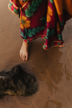 Close up of Indian woman's legs in traditional saree clothes on wet sand at ocean shore. Indian festival costume. Concept of solo tourism and travel to India. Part of a seriesの写真素材