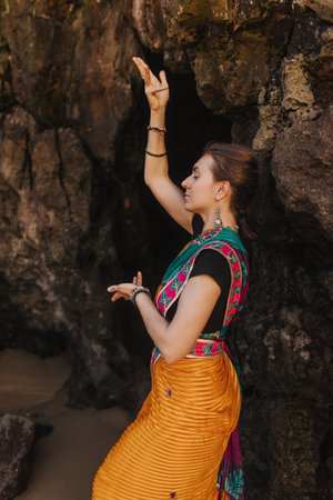 Indian woman in traditional saree clothes dances traditional dances on the nature with the ocean on background. Indian festival costume. Concept of solo tourism and travel to India. Part of a seriesの写真素材
