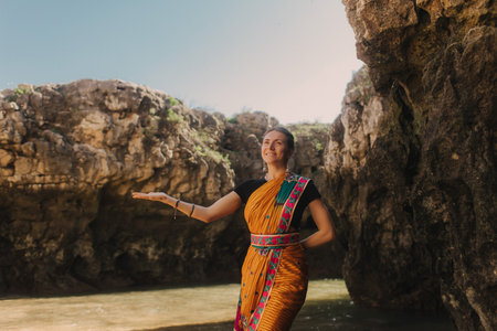 Indian woman in traditional saree clothes dances traditional dances on the nature with the ocean on background. Indian festival costume. Concept of solo tourism and travel to India. Part of a seriesの写真素材