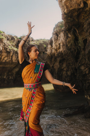 Indian woman in traditional saree clothes dances traditional dances on the nature with the ocean on...