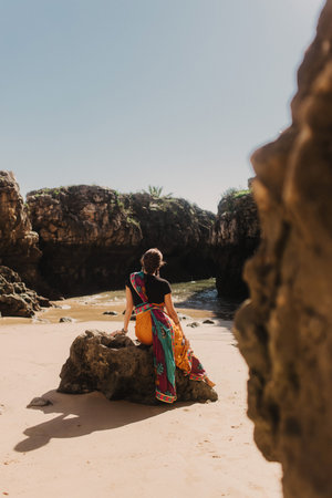 Indian woman in traditional saree clothes on the nature with the ocean on background. Indian festival costume. Concept of solo tourism and travel to India. Part of a seriesの写真素材