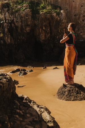 Indian woman in traditional saree clothes praying on the nature with the ocean on background. Indian festival costume. Concept of solo tourism and travel to India. Part of a seriesの写真素材