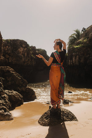 Indian woman in traditional saree clothes dances traditional dances on the nature with the ocean on background. Indian festival costume. Concept of solo tourism and travel to India. Part of a seriesの写真素材