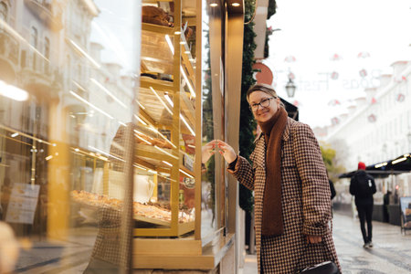 Gen Z middle age woman looking Portuguese egg tart pastry called Pastel de Nata in the window of a bakery in Lisbon. Solo tourism and travel. Part of a seriesの写真素材