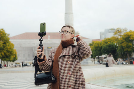 Vlogger traveler woman recording video on phone share via app her travel vacation in the Lisbon. Gen Z middle age woman influencer shooting social media stories on the street. Part of a series. UGCの写真素材